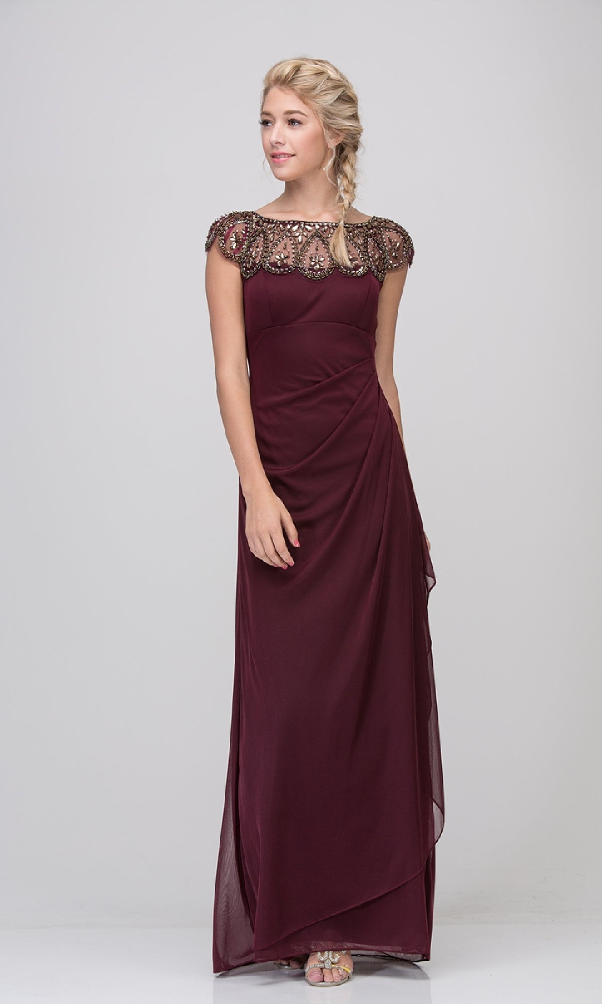 A woman wears the Cap-Sleeve Long Formal Dress: Eureka 3927, a floor-length evening gown featuring intricate beading and a sheer detailed neckline, set against a plain light background.